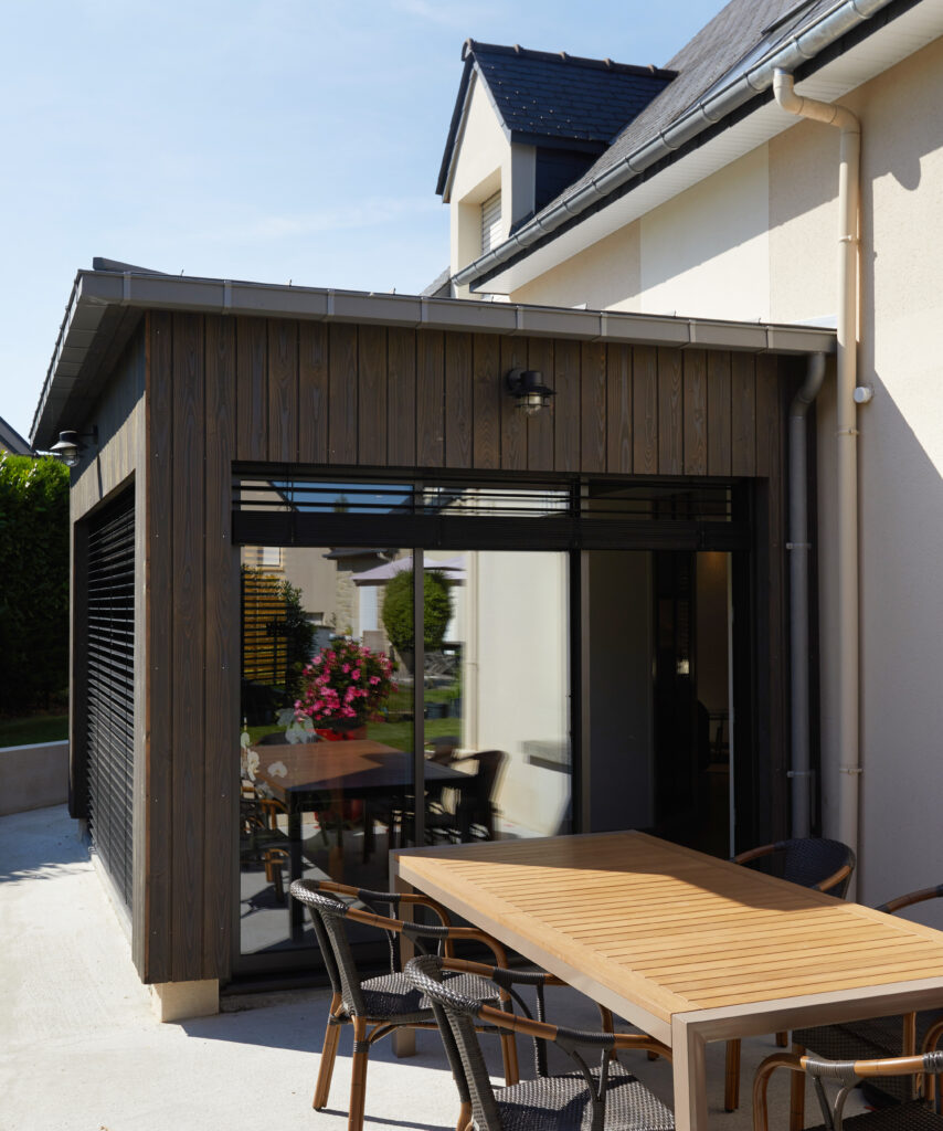 "Terrasse extérieure avec table en bois et chaises en rotin, extension en bois avec grandes fenêtres."