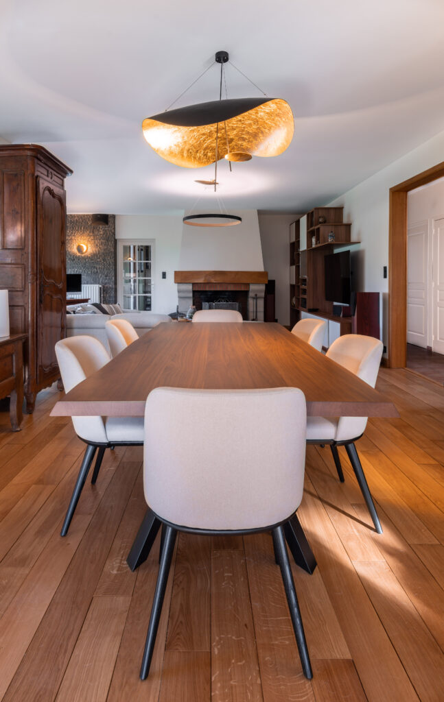 Salle à manger avec table en bois, chaises rembourrées et suspension lumineuse dorée au plafond