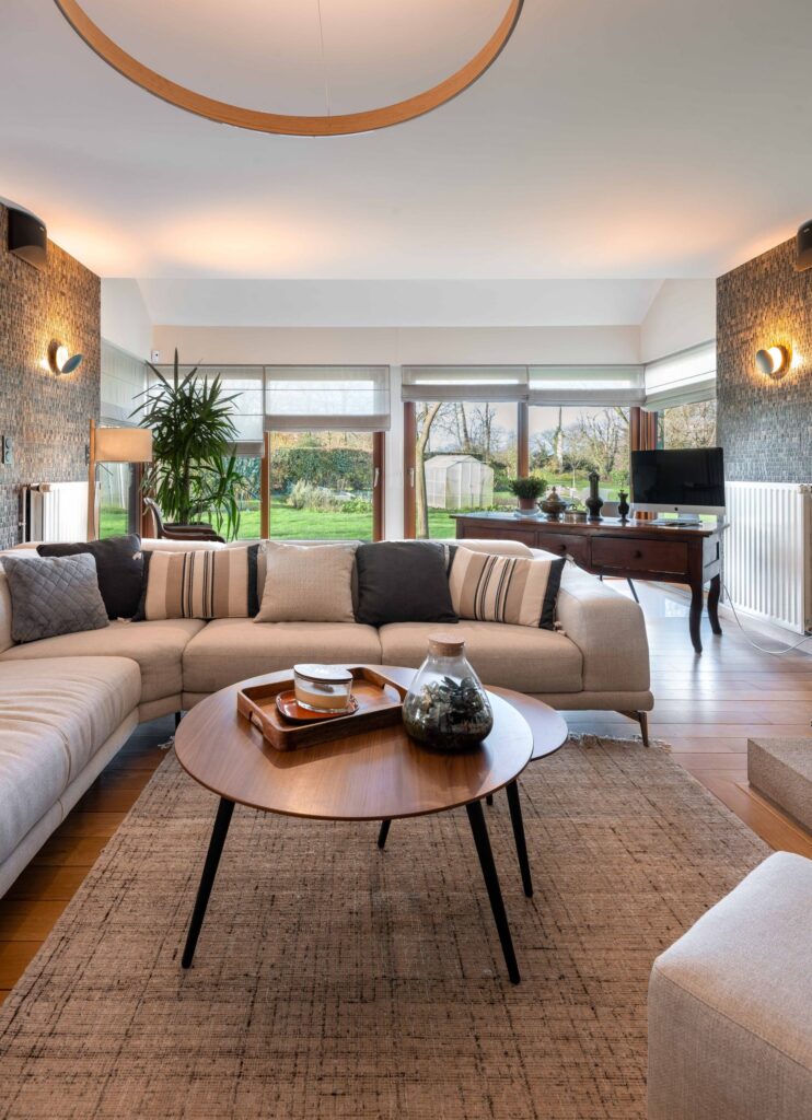 Salon contemporain avec un canapé beige, table basse en bois, grandes baies vitrées et vue sur le jardin.